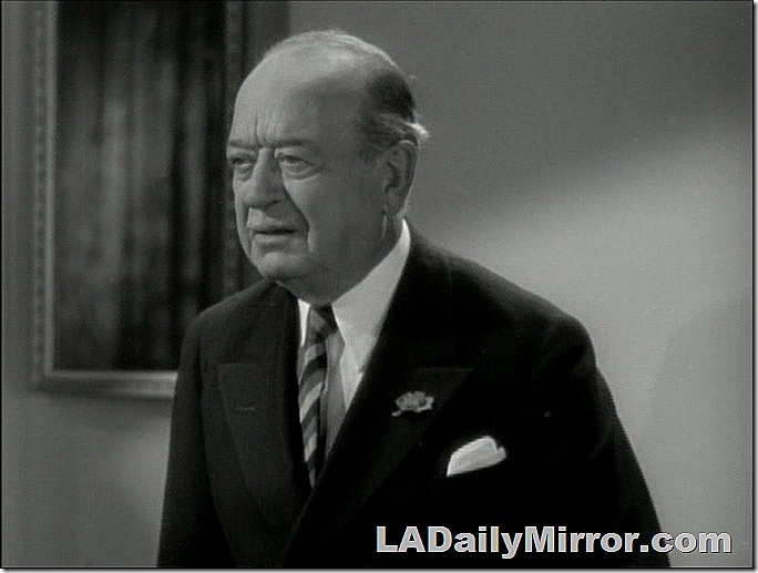 Balding man with slight mustache, wearing double-breasted suit and striped tie. 