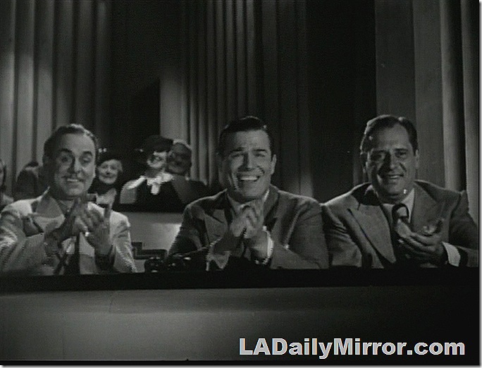 Three men in the balcony of a theater. They are applauding. 