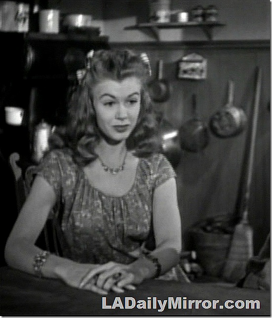 Young woman with long hair sitting at a table with her hands folded. 