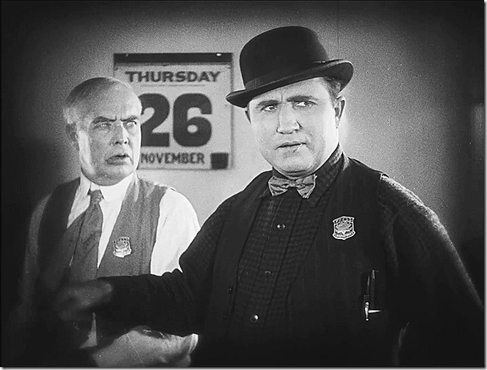 Man in derby with small bowtie, wearing a badge. Another man in a tie and vest looks at him. Man in derby with small bowtie, wearing a badge. Another man in a tie and vest looks at him.