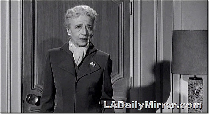 Older woman in tasteful suit, hair pulled back, a scarf at her neck. She does not approve of such goings-on. 