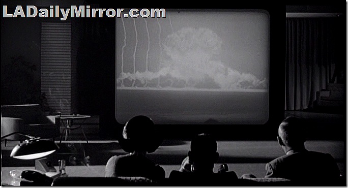 POV shot of three people silhouetted watching a movie of an atomic bomb explosion. 