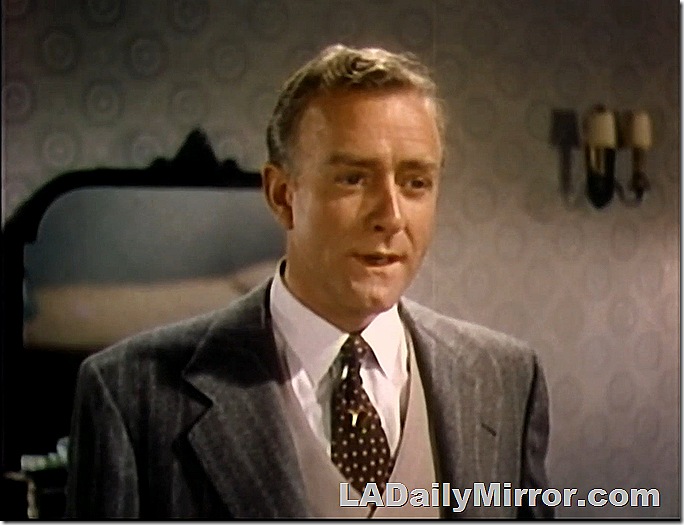 Man in coat, vest and tie. A mirror is in the background. 