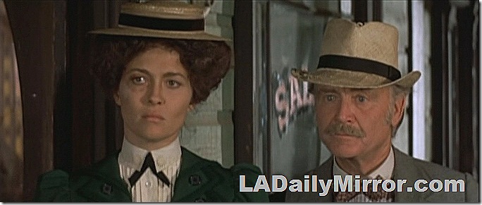 Man with mustache, wearing hat, coat and bowtie. 