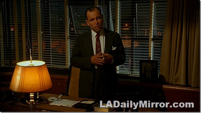 Man standing at desk with background visible through venetian blinds. 