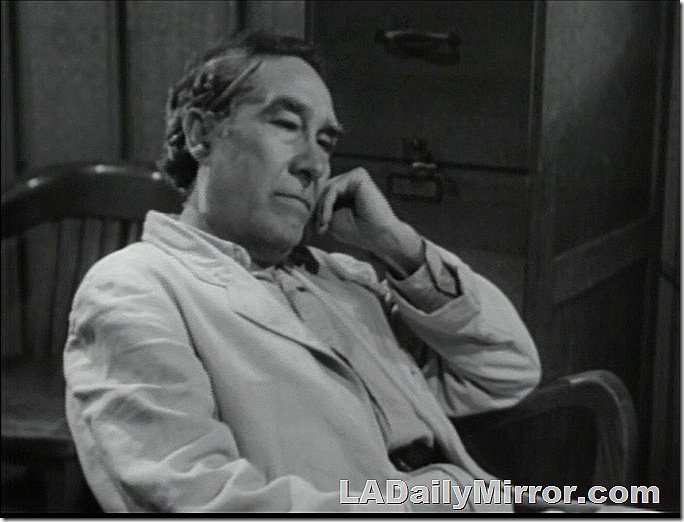 Man in light-colored suit sitting with his head resting on his hand. 