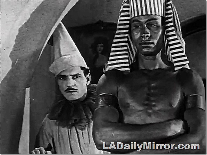 Man in clown outfit next to man in Egyptian costume. 