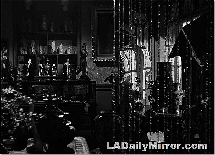 Man in shop full of Asian figurines. He is wearing a hat and carrying a gun. 