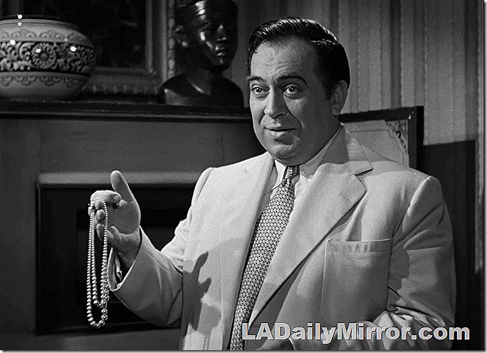 Man in white suit holding a pearl necklace. 