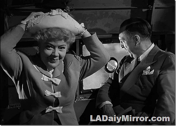 Woman adjusting her hat as a man looks out the window. 