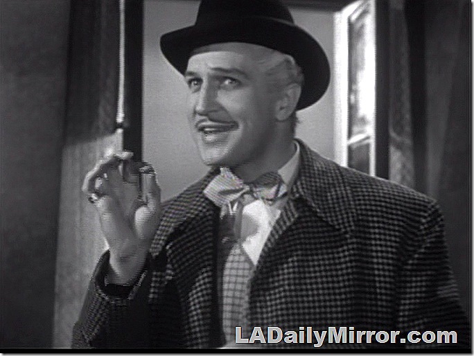 Man in hat and checked coat making a hand gesture. 