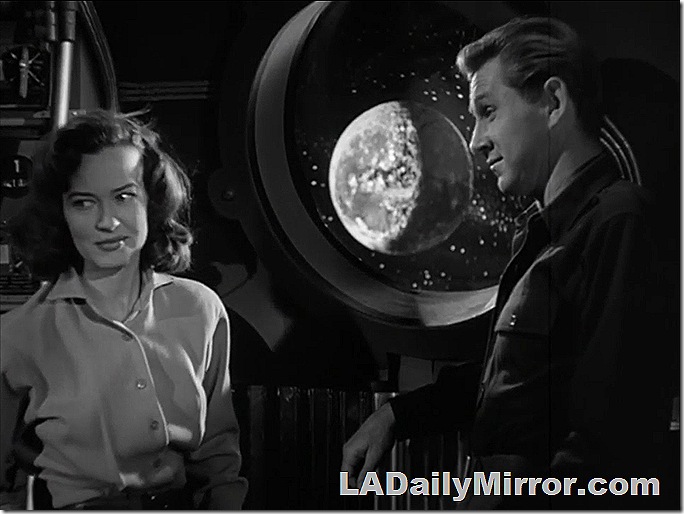 Man and woman in spacecraft with a planet and stars visible out the portal. 