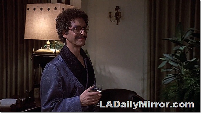Man with glasses, a mustache and curly hair carrying a martini. 