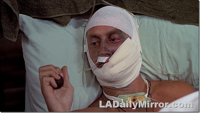Man in hospital bed with his entire head shrouded with bandages. 