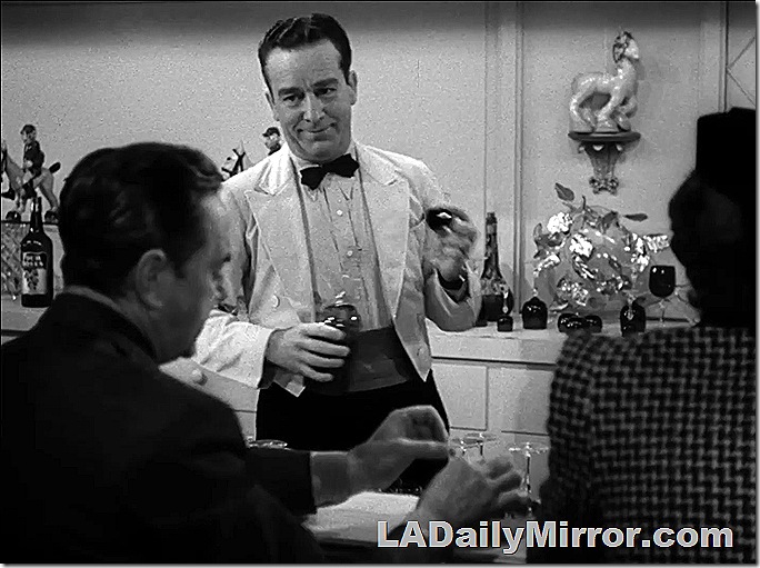 Bartender mixing drinks for customers. He's wearing a coat, a cummerbund and a bow tie. 