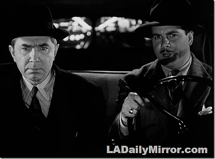 Two men riding in a car. They are wearing hats and suits. 