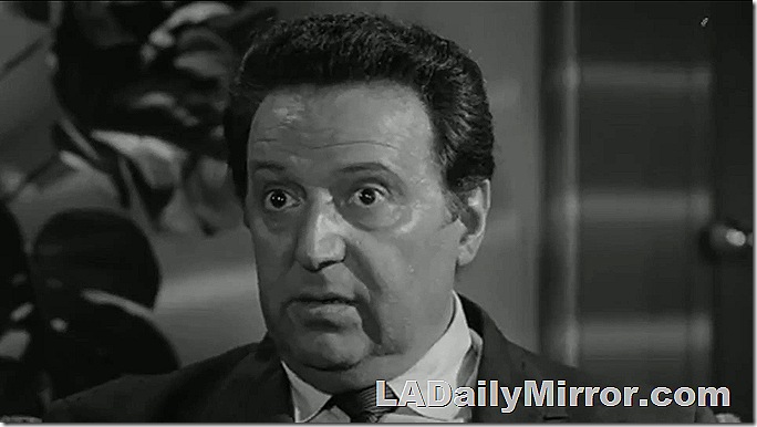 Man with coat and tie, hair combed straight back. He seems surprised. 