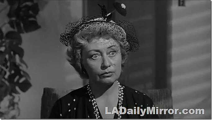 Woman with shortish hair, a silly hat, a necklace and an amazed expression. 