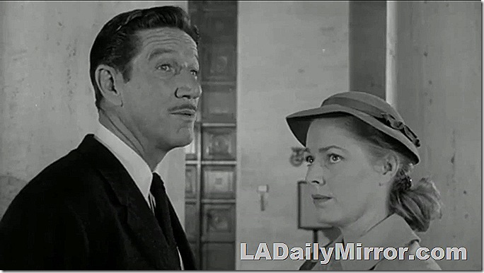 Man in coat and tie, with a slight mustache, talking to a woman in a plain coat and plain hat. 