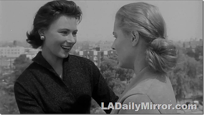 Woman with stylish dark hair, earrings and a fashionable dress, talking to Back of the Head Woman. A skyline is in the background. 