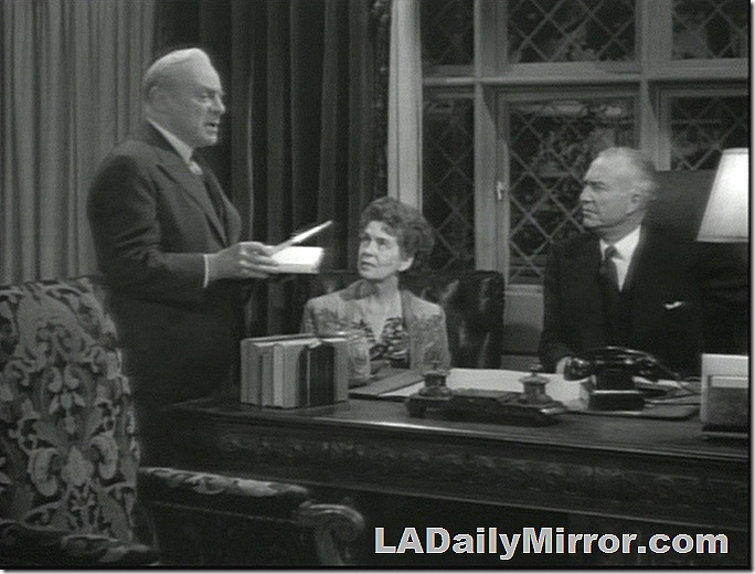 Man and woman sitting at desk look at man standing next to desk holding a book. Man and woman sitting at desk look at man standing next to desk holding a book.