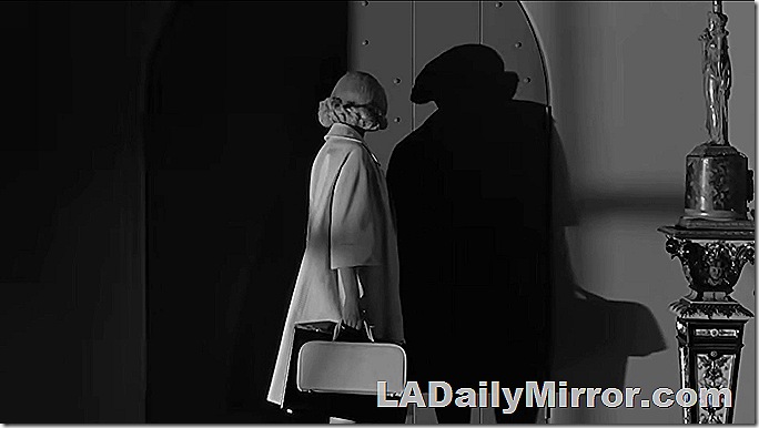 Nighttime shot of woman in coat with flip hairdo and half-length sleeves facing a door and casting a shadow. She holds a purse and a suitcase. Nighttime shot of woman in coat with flip hairdo and half-length sleeves facing a door and casting a shadow. She holds a purse and a suitcase.