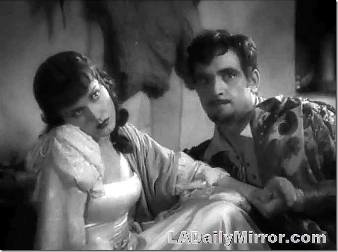 Woman in white dress, head resting on her shoulder, and a man with a mustache and slight beard. 