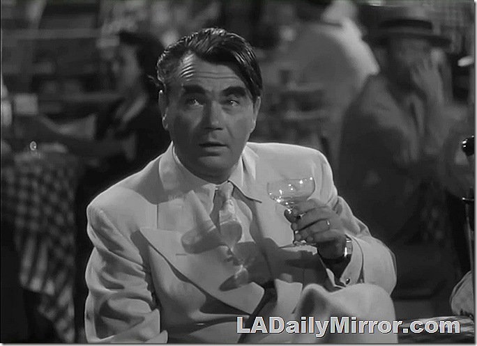 Man in white double-breasted suit, sitting at a table, having a cocktail. 