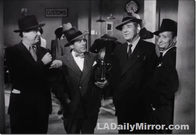 Four men in suits and hats. One carries a camera and wears a bow tie. Four men in suits and hats. One carries a camera and wears a bow tie.