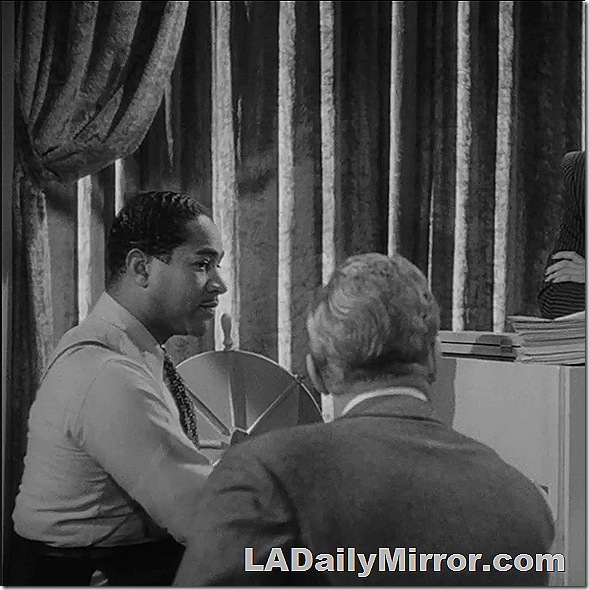 Man in shirtsleeves, suspenders and a tie sitting at an upright piano. 