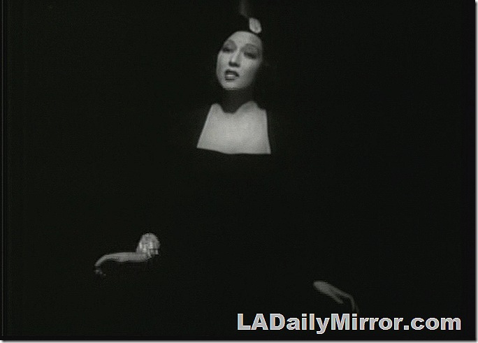 Woman singer in black outfit, blacked out so only her face, chest and hands show. 