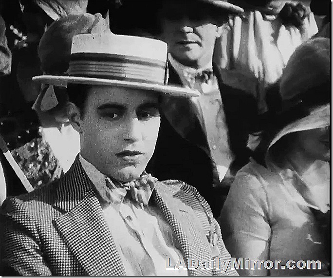 Man in coat, bow tie and straw hat. 