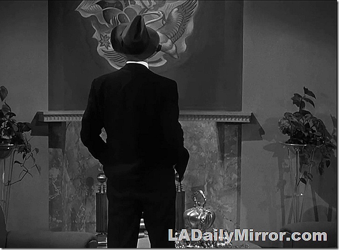 Man looking at a picture on the wall. We see his back. He's wearing a hat. Man looking at a picture on the wall. We see his back. He's wearing a hat.